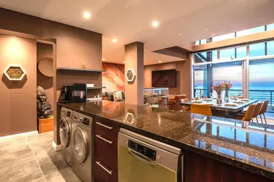 a kitchen and dining room with a view of the ocean at Serviced Beach Penthouse, 100k Gemstone display, All Ensuite in Cape Town