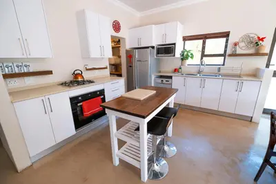 a kitchen with white cabinets and a wooden table at La Haven Self Catering in Hermanus