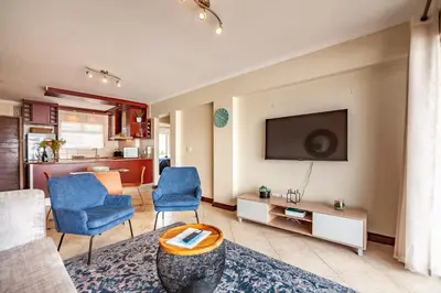 a living room with a couch and chairs and a tv at Beachfront 3rd floor 2 bedroom w communal swimming pool- B16 Blouberg in Bloubergstrand