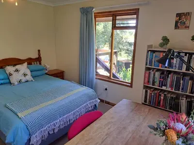 a bedroom with a bed with a table and a window at Helderberg Cottage in Somerset West