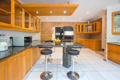 a kitchen with wooden cabinets and a counter with stools at Suikerbos Guesthouse in Cape Town