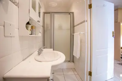 a white bathroom with a sink and a shower at Suikerbos Guesthouse in Cape Town