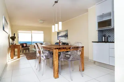 a kitchen and dining room with a wooden table and chairs at Sea Spray A308 in Bloubergstrand