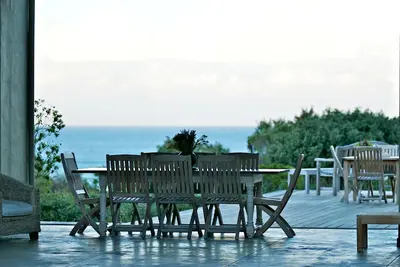 a wooden table and chairs on a deck with the ocean at Mosselberg on Grotto Beach in Hermanus