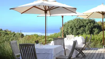 a table with chairs and an umbrella on a patio at Mosselberg on Grotto Beach in Hermanus
