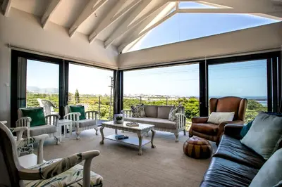 a living room with couches and chairs and large windows at Vue La Mer in Hermanus