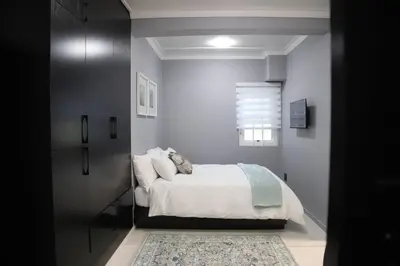 a bedroom with a bed with white sheets and a rug at Trendy Cottage Hideaway in Cape Town