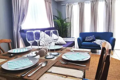 a dining room table with wine glasses and a blue couch at Ocean Escape in Strand