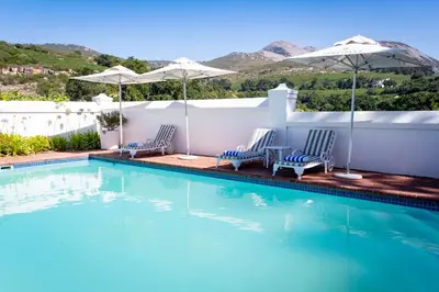 a swimming pool with two chairs and umbrellas at Laborie Jonkershuis in Paarl