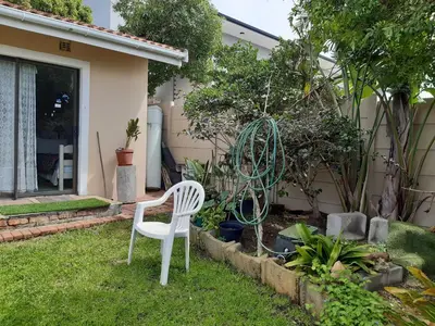 a white chair in the yard of a house at Cosy studio garden cottage in Cape Town