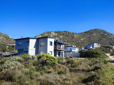 a house on a hill with mountains in the background at Prinia on Peak holiday home in Pringle Bay