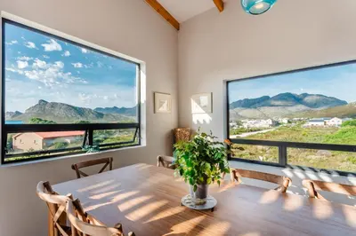 a dining room with a table and two large windows at Prinia on Peak holiday home in Pringle Bay