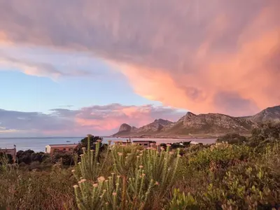 a rainbow in the sky over a beach with mountains at Prinia on Peak in Pringle Bay in Pringle Bay