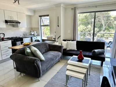 a living room with a couch and a kitchen at Cozy Rondebosch Apartment in Cape Town