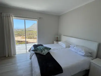 a white bedroom with a large bed with a window at Die Steenhuisie in Pringle Bay