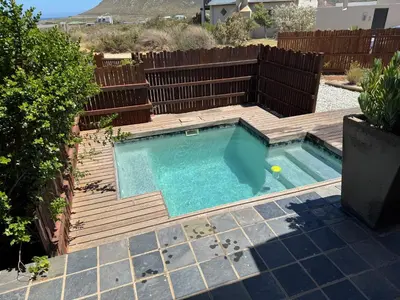 a swimming pool with a wooden deck and a swimming poolvisor at Die Steenhuisie in Pringle Bay