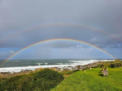 a rainbow over a beach with the ocean at Brunia Bay Apartment in Hermanus