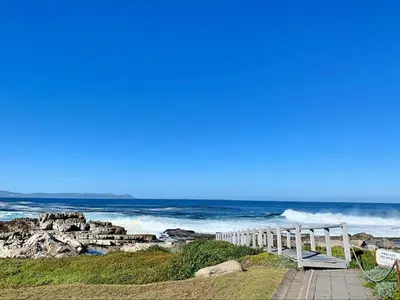 a white bench sitting on the side of a beach at Refresh at 50 Whale Rock in Hermanus
