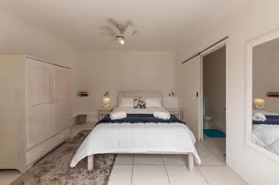 a white bedroom with a bed and a ceiling fan at 'Seagul Cove', Private Villa on the beach, Sleeps 7 in Cape Town