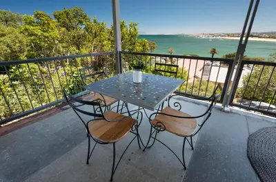 a table and chairs on a balcony with the ocean at 'Seaside Cottage', Sleeps 4 with a 3 minute walk from the beach! in Cape Town