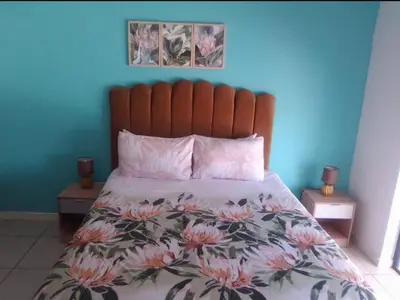 a bedroom with a bed with a floral comforter and two tables at The Sandown Blouberg self catering unit in Parklands