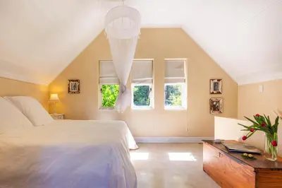 a bedroom with a large bed and two windows at Devon Castle Orchard Cottage in Stellenbosch