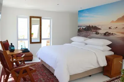 a bedroom with a white bed with a painting on the wall at Nivenia Beach House in Bettyʼs Bay