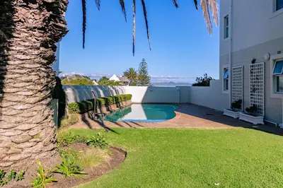 a palm tree next to a building with a swimming pool at Seaside Serenity: Tranquil Oceanview Retreat in Hermanus