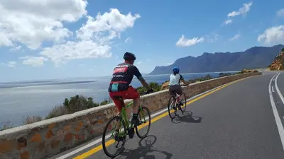 two people riding bikes on a road near the water at Cardamom Cottage, sleeps 3 and 1 min walk to beach in Cape Town