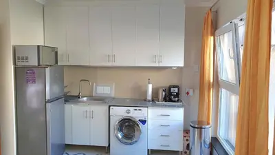 a kitchen with a washing machine and white cabinets at Hidden gem on Eksteen in Cape Town