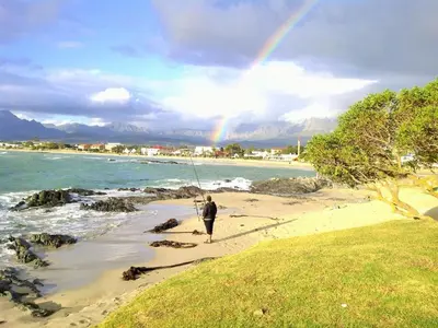 a person fishing on the beach with a rainbow in the sky at Loft Cottage, sleeps 2. Central and Cozy! in Cape Town
