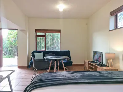 a bedroom with a bed and a table and a couch at Loft Cottage, sleeps 2. Central and Cozy! in Cape Town