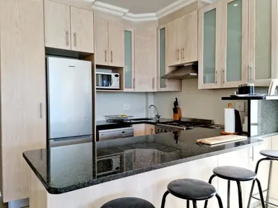 a kitchen with wooden cabinets and black counter stools at Beach Apartment on Bikini Beach - sleeps 4 in 2 Ensuite Bedrooms in Cape Town