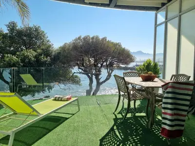 a patio with a table and chairs and a view of the water at Beach Apartment on Bikini Beach - sleeps 4 in 2 Ensuite Bedrooms in Cape Town