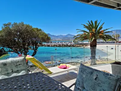 a patio with a view of a beach and the ocean at Beach Apartment on Bikini Beach - sleeps 4 in 2 Ensuite Bedrooms in Cape Town