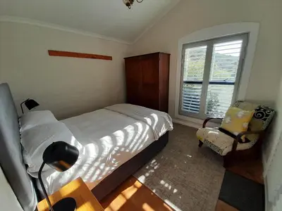 a bedroom with a bed and a window and a chair at Peaceful Seaside Cottage, Betty's Bay Accommodation in Clareport