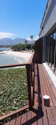 a wooden bench sitting on the side of a beach at Driftwood Beach Villa in Gordonʼs Bay