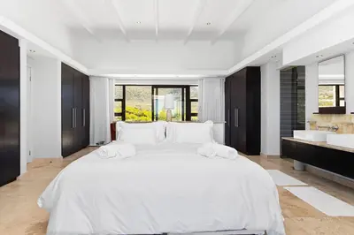 a white bedroom with a large white bed and a sink at Hangklip Villa in Pringle Bay