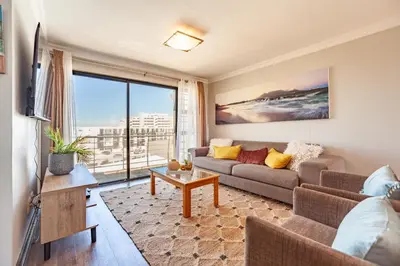 a living room with a couch and a large window at Luxury 3 bedroom Duplex Penthouse with communal swimming pool in Bloubergstrand
