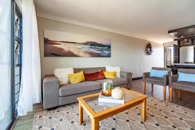 a living room with a couch and a table at Luxury 3 bedroom Duplex Penthouse with communal swimming pool in Bloubergstrand