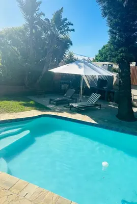 a blue swimming pool with a umbrella and a bench at Tranquil Pool View in Cape Town