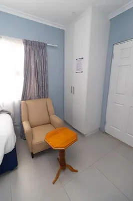 a bedroom with a chair and a table and a bed at Malaika Guest House in Cape Town