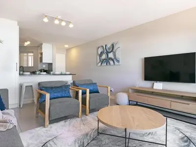 a living room with a tv and chairs and a table at Zeezicht 204 Bloubergstrand in Bloubergstrand