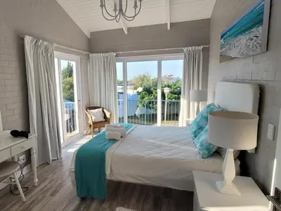 a bedroom with a bed and a desk and windows at Nest Egg Holiday Home Voëlklip in Hermanus