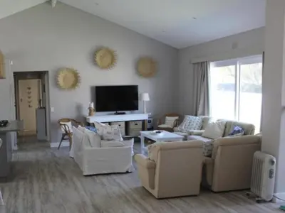 a living room with white furniture and a flat screen tv at Nest Egg Holiday Home Voëlklip in Hermanus