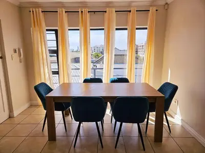 a dining room table with chairs and a large window at Strand Beach Apartment in Cape Town