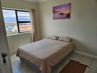 a small bedroom with a bed and a window at Strand Beach Apartment in Cape Town