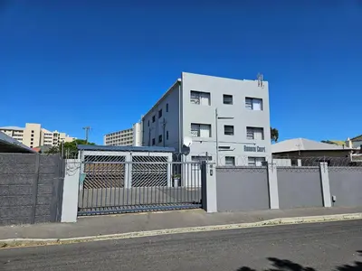 a white building with a gate in front of a fence at Strand Beach Apartment in Cape Town