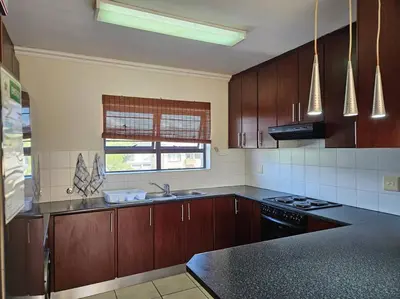 a kitchen with wooden cabinets and a black counter top at Strand Beach Apartment in Cape Town