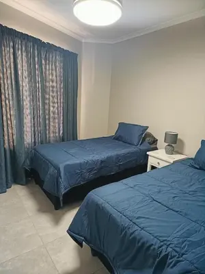 a bedroom with two beds and a window with blue sheets at Nautica3 in Cape Town